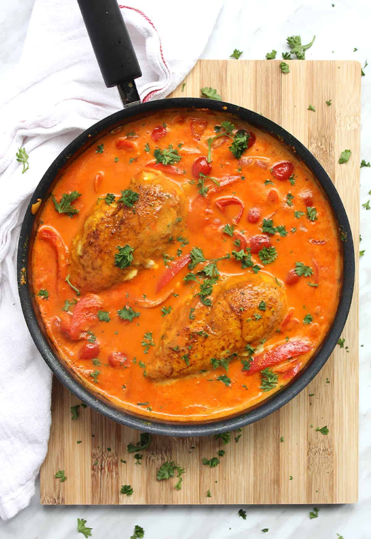 The cooked dish in a skillet on a wooden chopping board