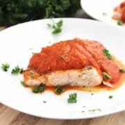Salmon served with red pepper sauce on a white plate