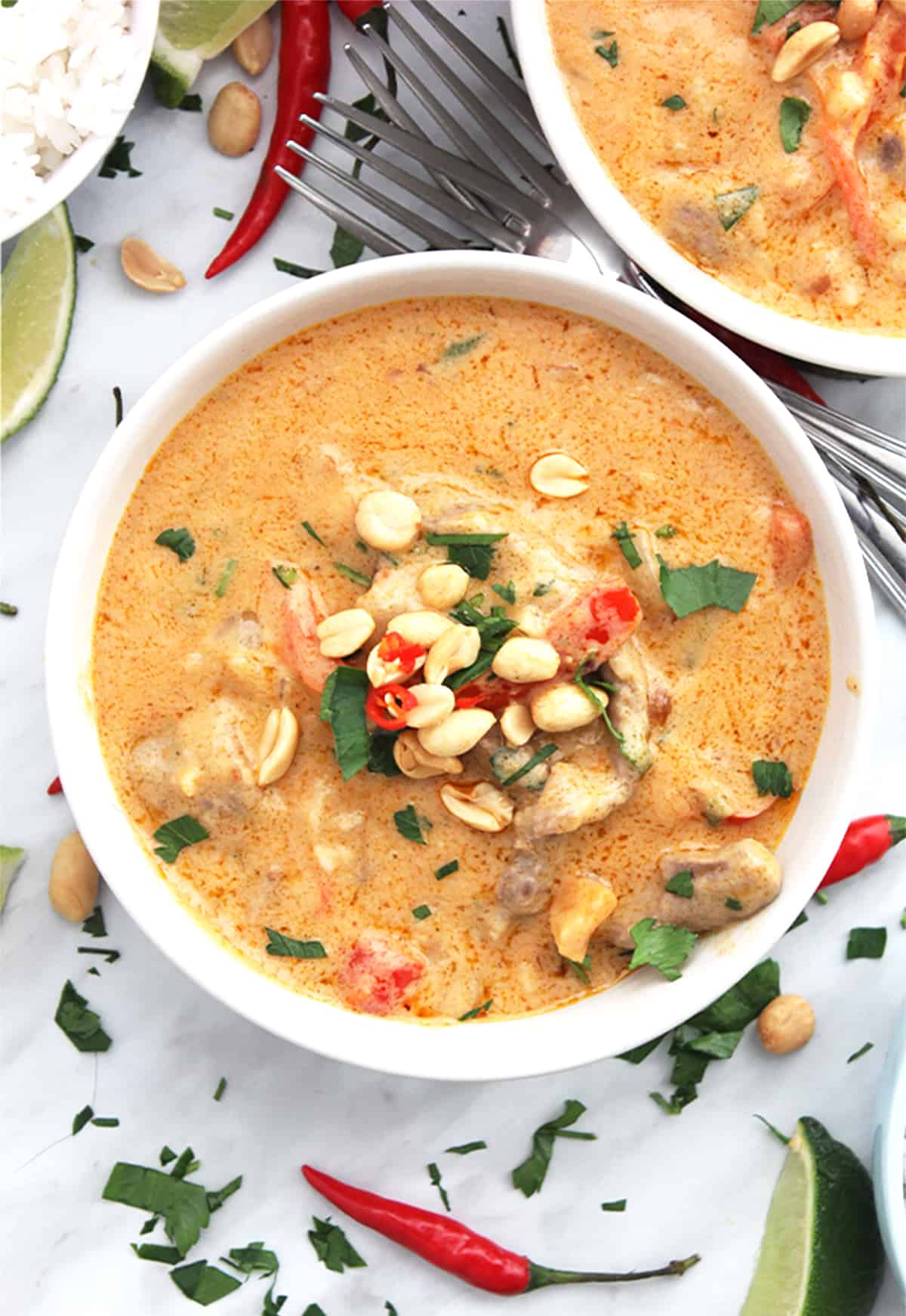 The curry in a white bowl topped with fresh chili, coriander and peanuts.