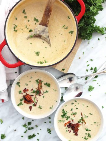 Two bowls of roasted cauliflower soup topped with bacon and herbs