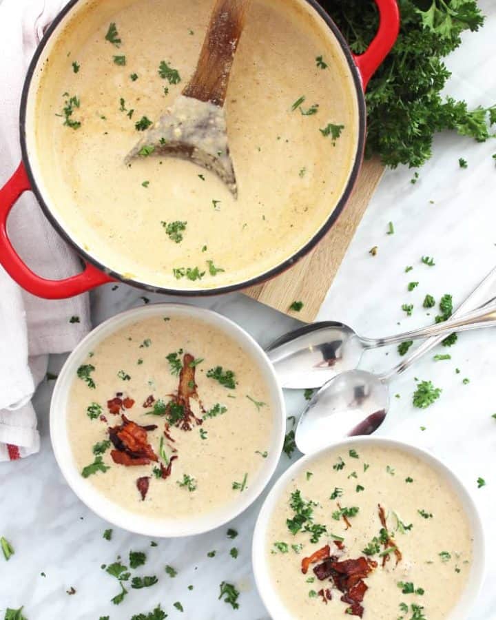 Two bowls of roasted cauliflower soup topped with bacon and herbs