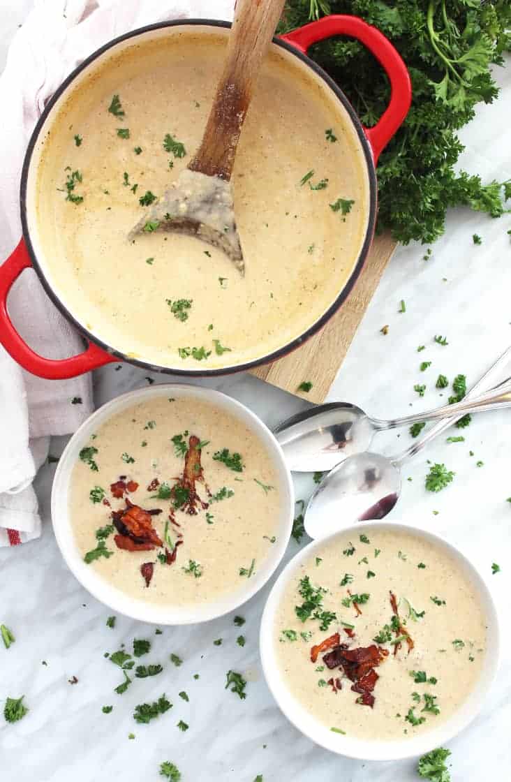 Two bowls of roasted cauliflower soup topped with bacon and herbs