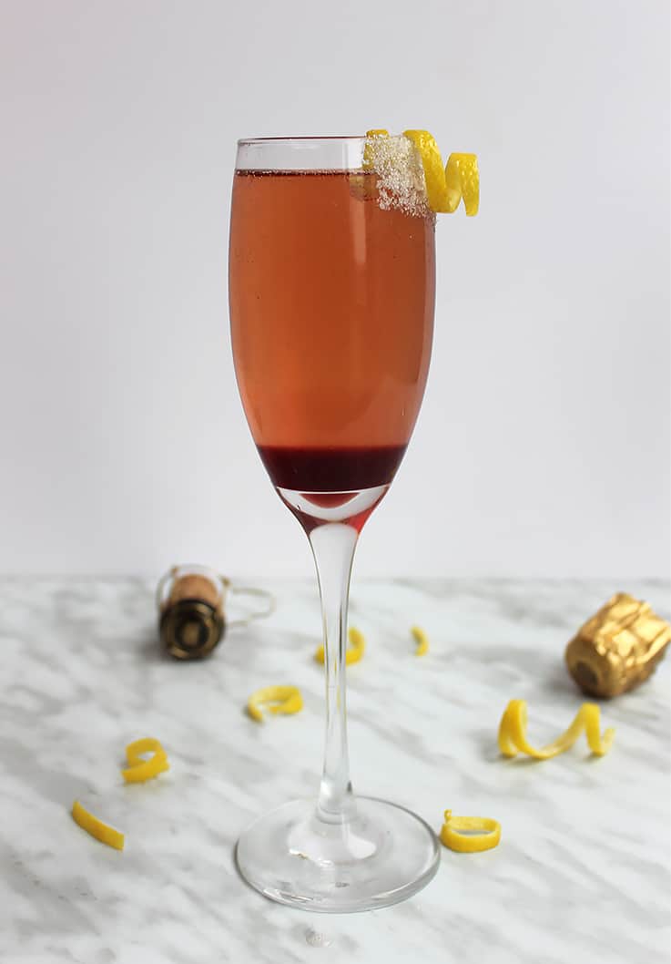 A cherry champagne cocktail next to a champagne cork