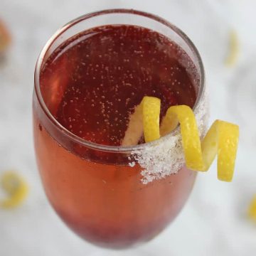 A cherry champagne cocktail with a sugar rim and lemon garnish
