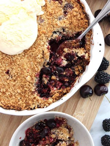 The baked crumble in a pie dish being served into a bowl with a spoon