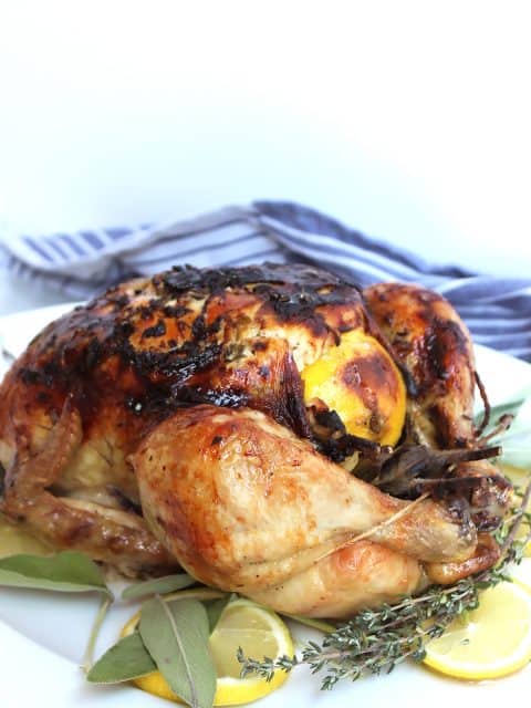 Roast chicken on a white platter with lemon and herbs