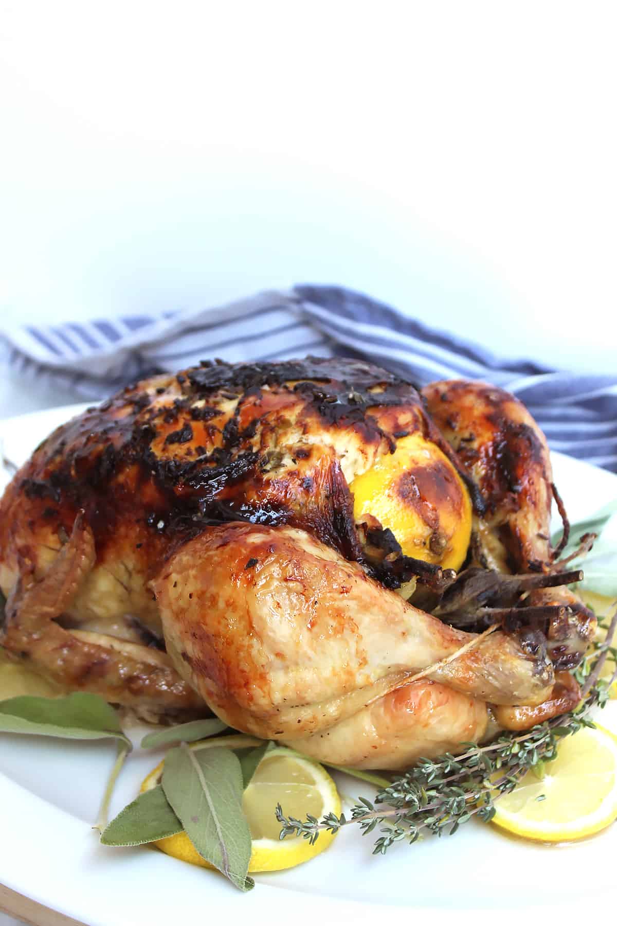 Roast chicken on a white platter with lemon and herbs