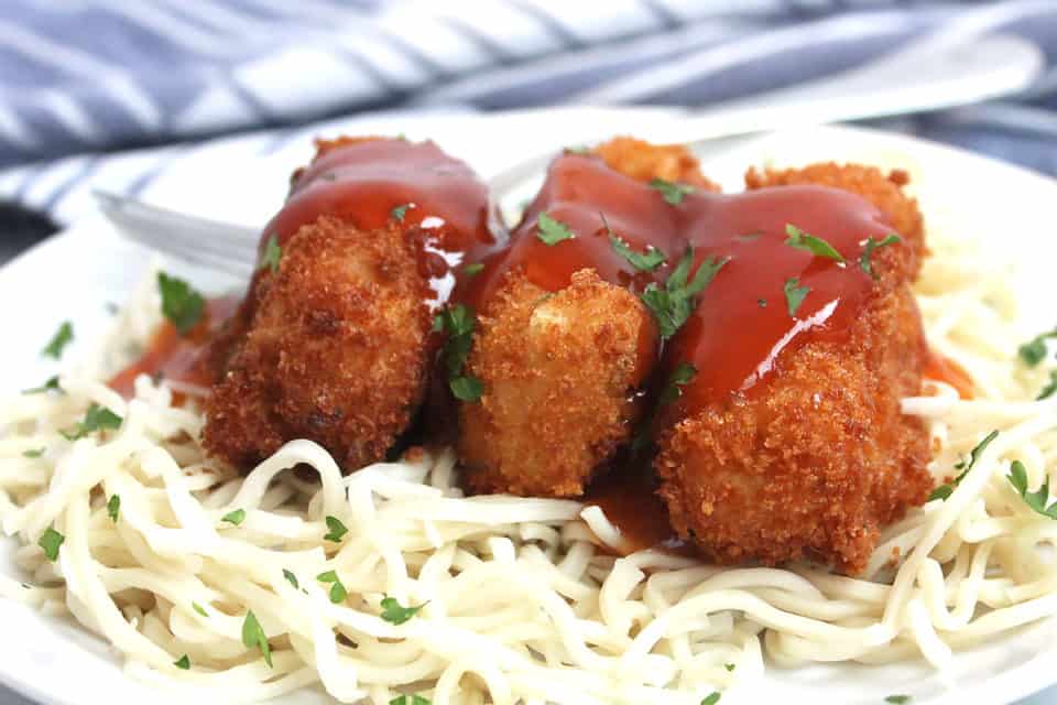 Three pieces of breaded tofu on boodles and drizzled with sauce
