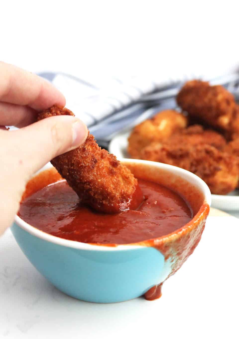 A breaded tofu stick being dipped in a red sauce