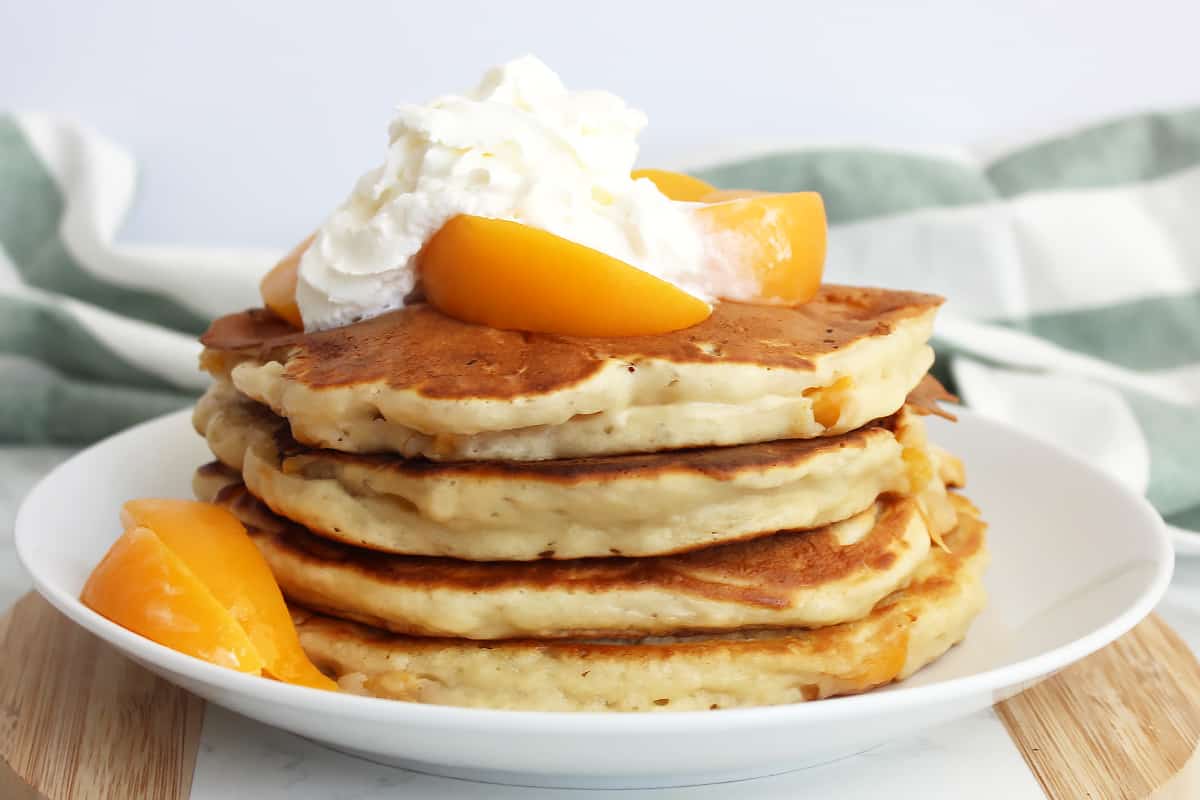 A stack of peach pancakes topped with whipped cream and peach slices