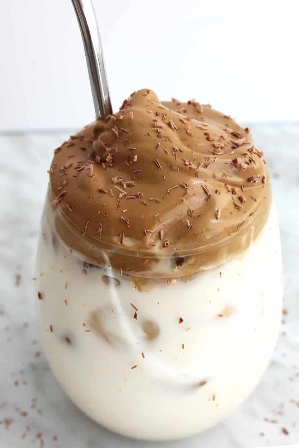 Whipped coffee ontop of a glass of milk with a metal straw