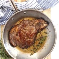 The steak being fried in a pan with fresh thyme