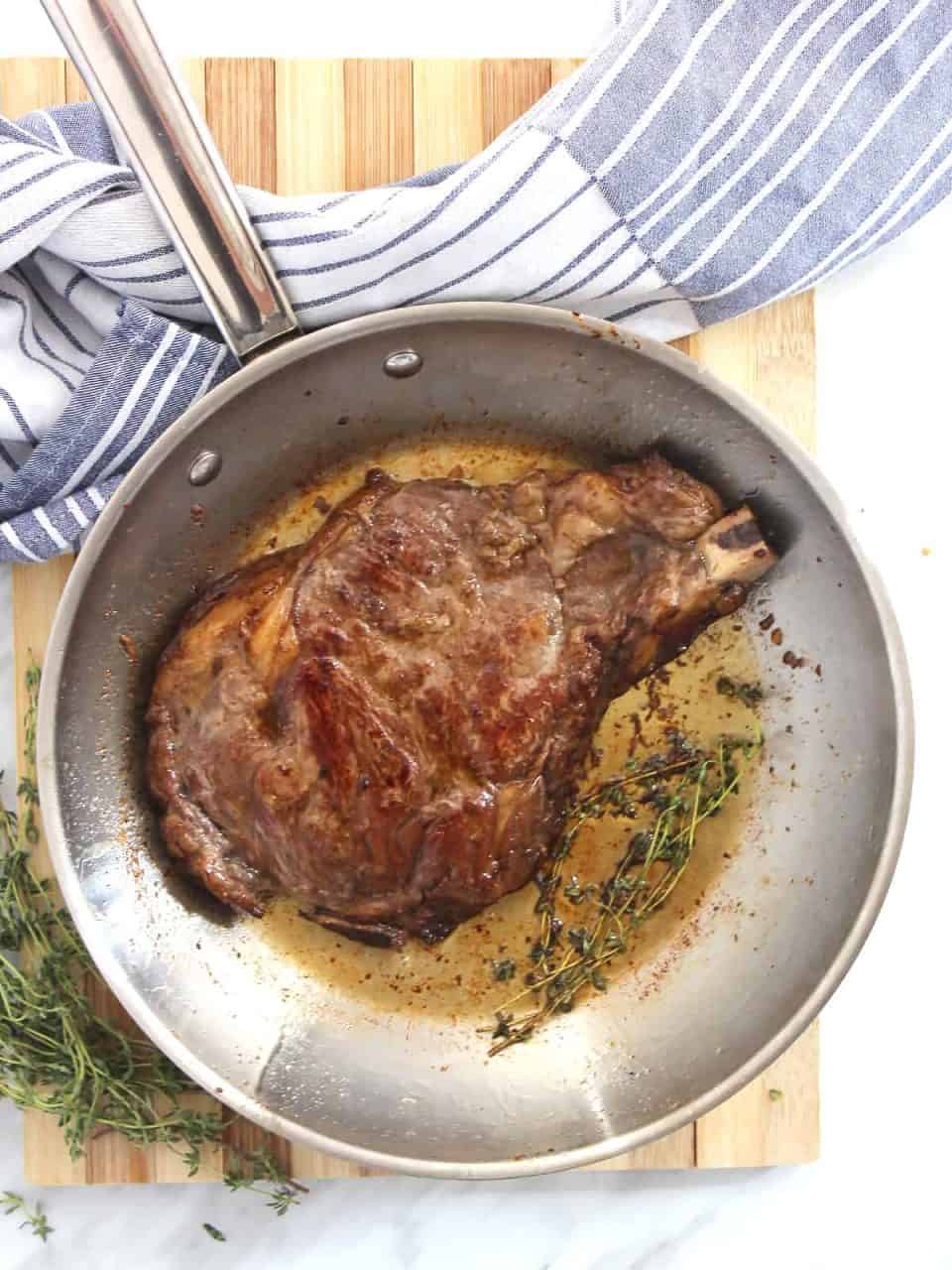 The steak being fried in a pan with fresh thyme