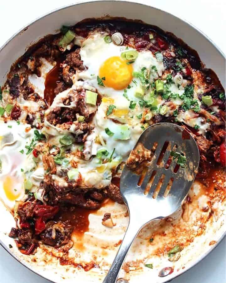 Beef and egg shakshuka being served out of a skillet with a slotted spoon
