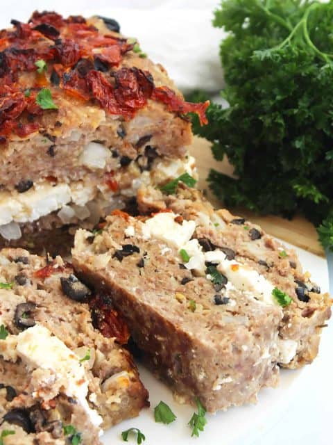 Two slices of lamb meatloaf on a chopping board garnished with fresh parsley.