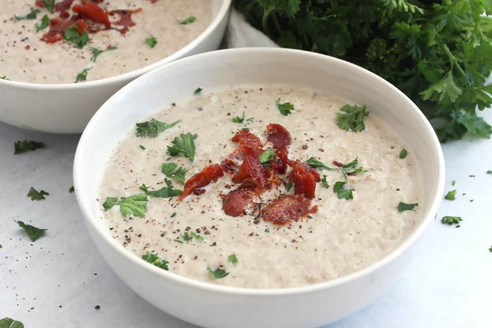 A bowl of soup garnished with bacon bits and fresh herbs