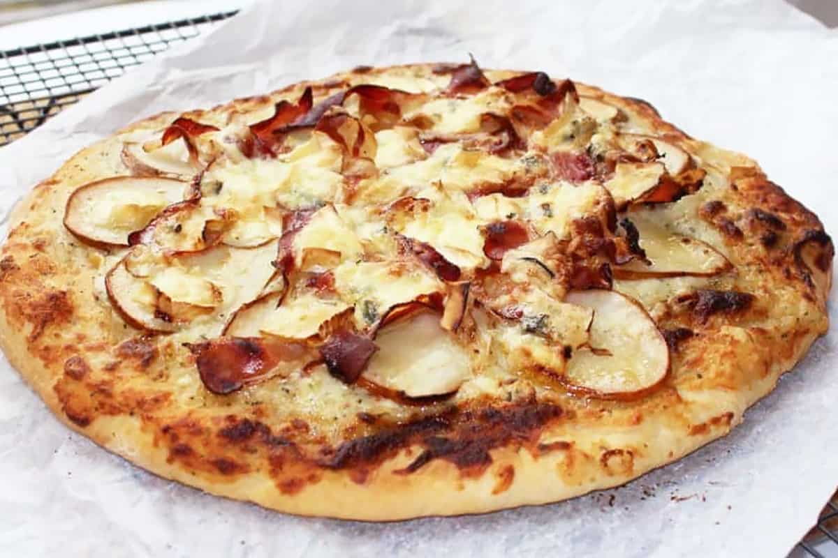 White pizza topped with pears and ham on a piece of parchment paper
