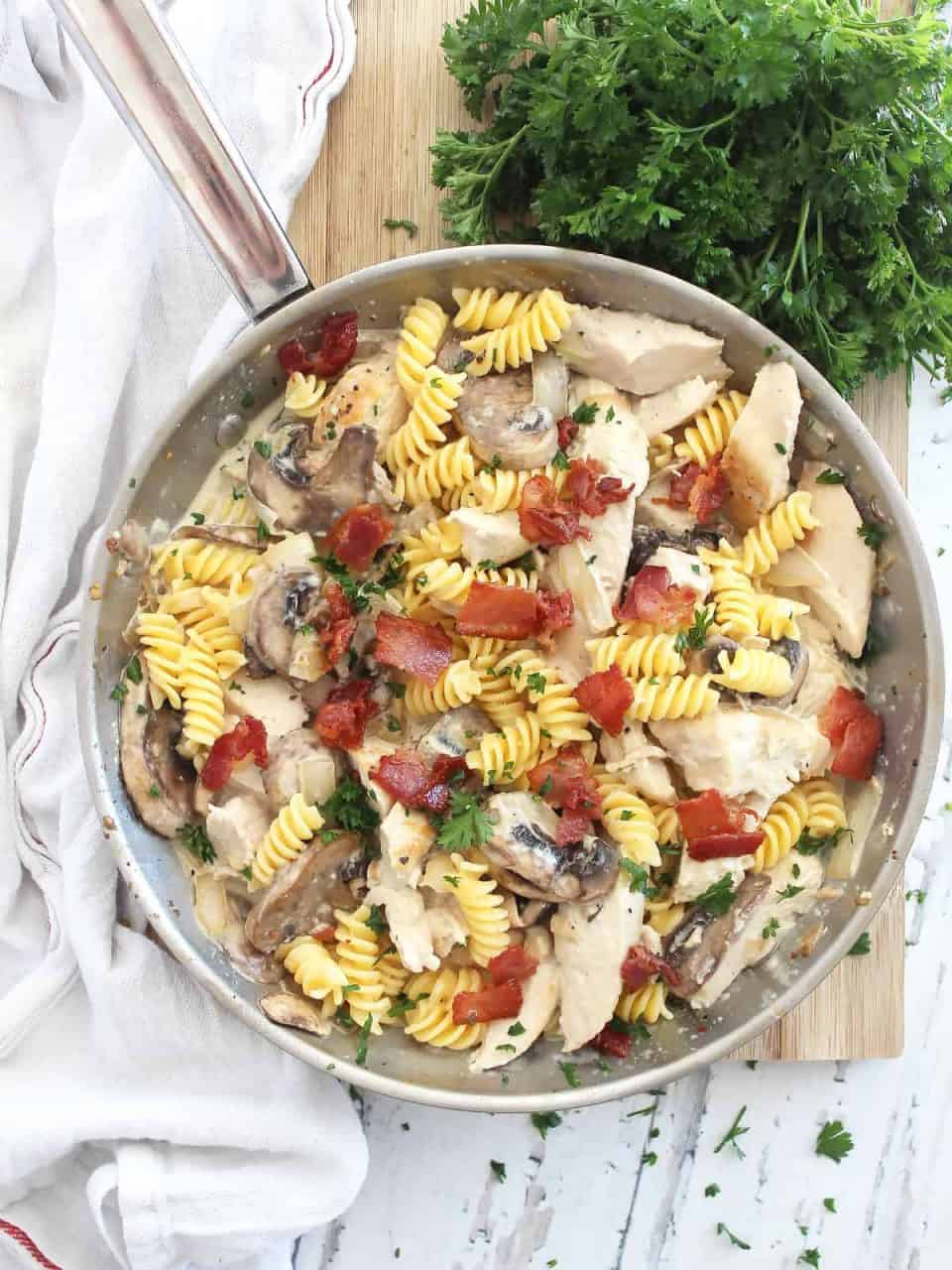 Overhead shot of chicken mushroom pasta in a skillet garnished with fresh herbs.