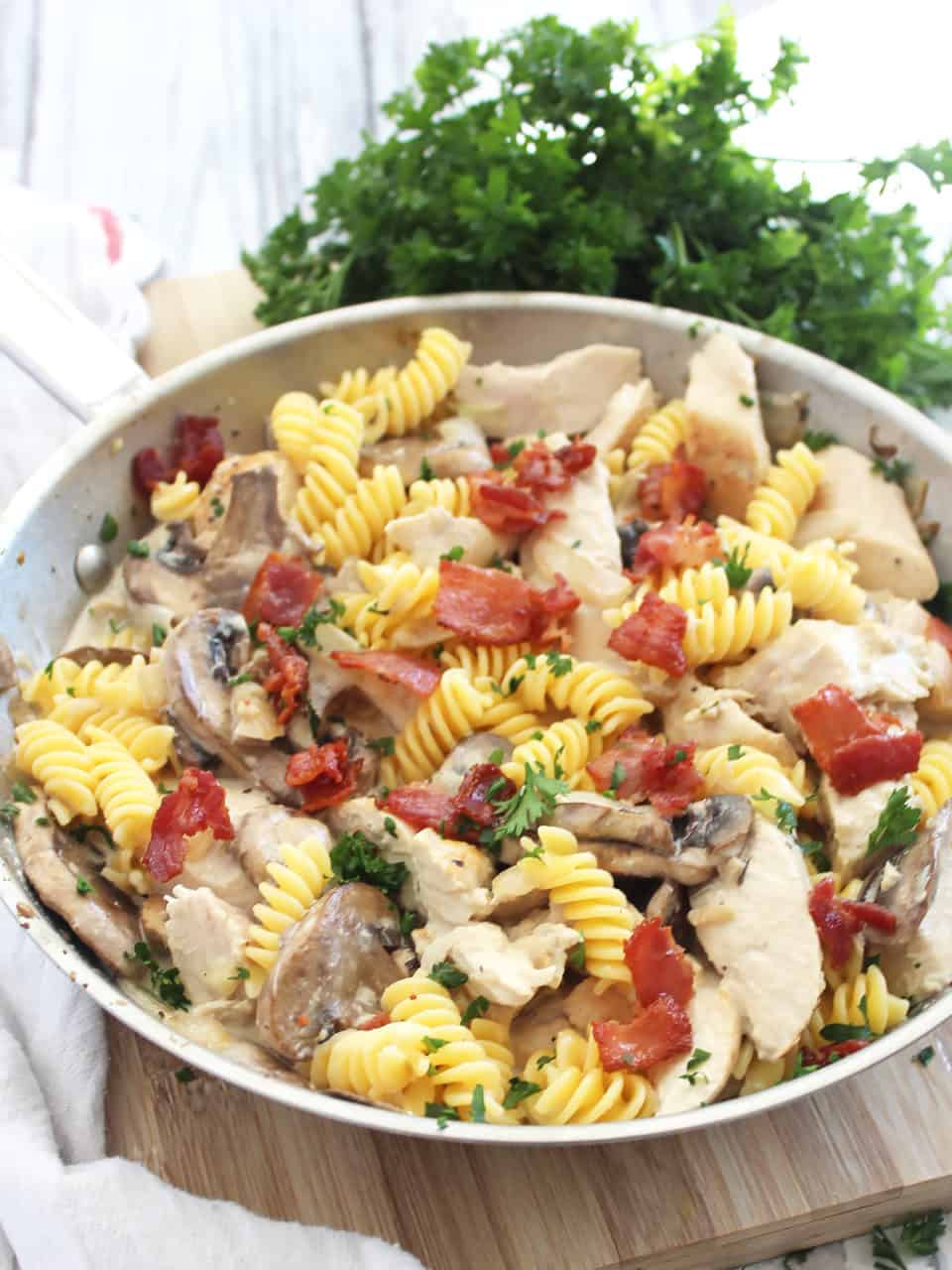 Chicken and mushroom pasta topped with bacon pieces in a silver skillet.