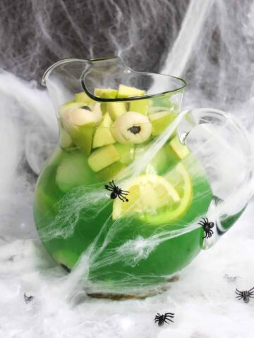 Halloween sangria in a large jusg decorated with cobwebs and plastic spiders.