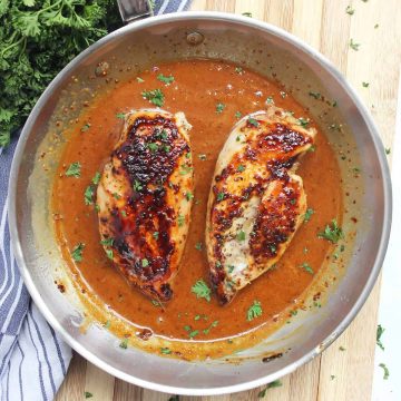 Overhead shot of the honey and mustard chicken breasts in a skillet and garnished with fresh herbs.