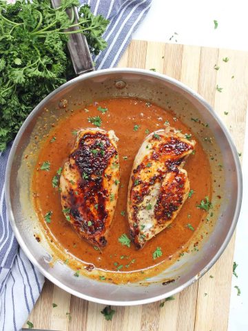 Two chicken breasts in honey and mustard sauce in a skillet.
