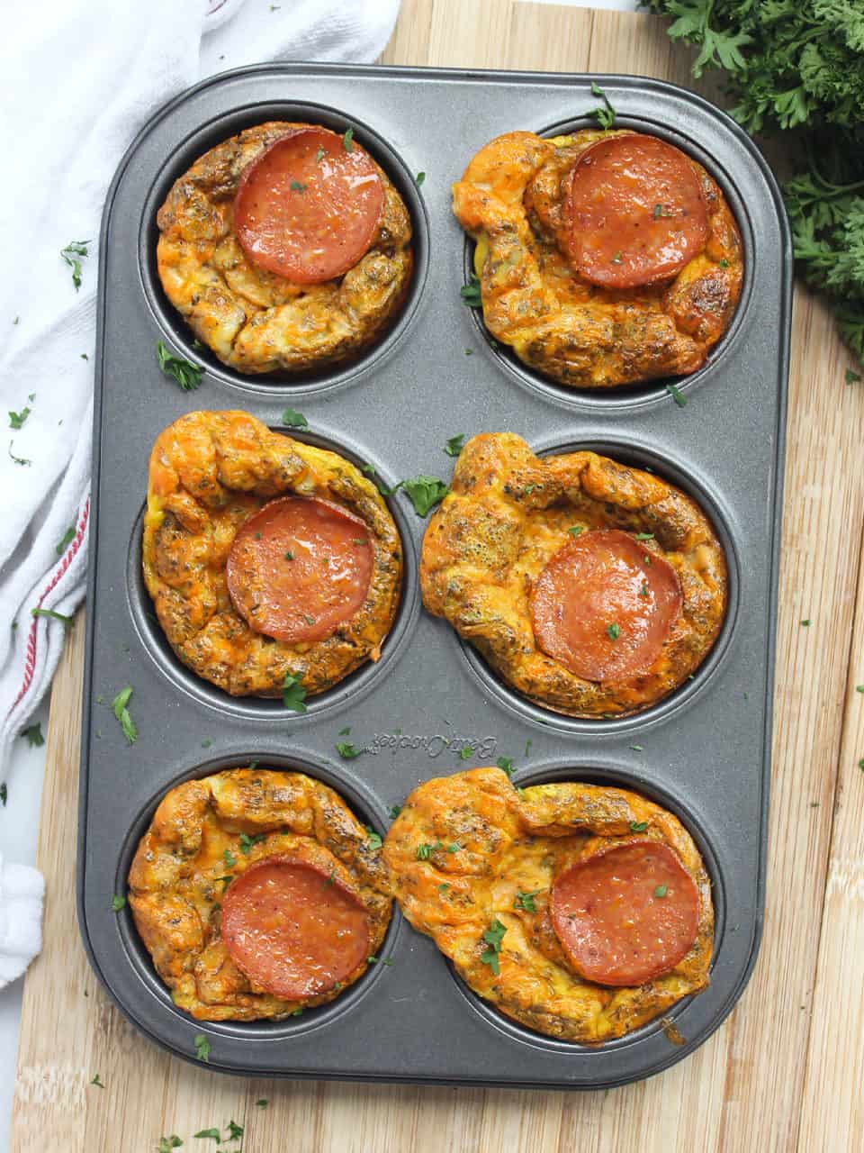 Six baked pizza egg bites in a muffin tin.