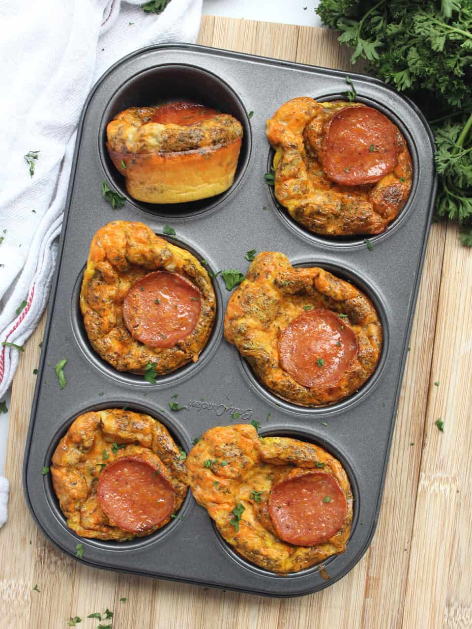 Six pizza egg bites in a muffin tin with one turned on it's side.