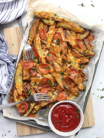 A baking sheet with the pizza fries served with two forks and a ramekin of ketchup.