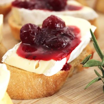 Close up of a brie and cranberry crostini next to fresh rosemary.