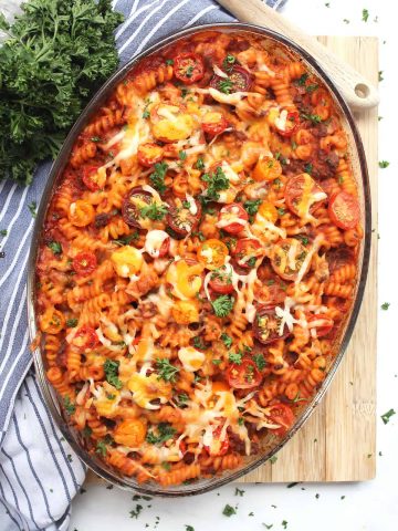 Baked ground beef pasta bake in a glass dish on a wooden chopping board.