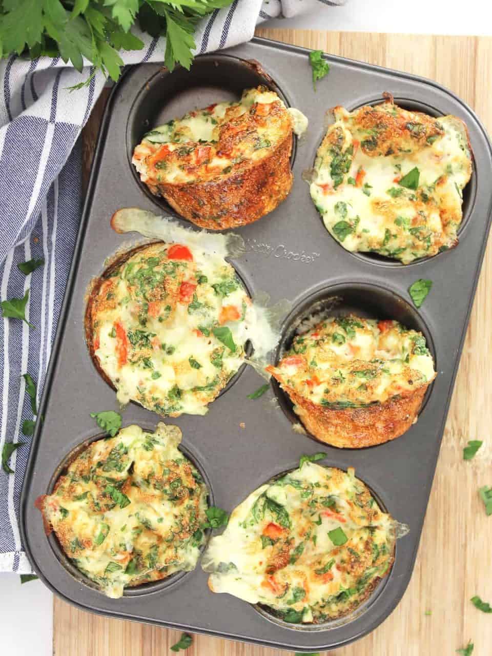 Overhead shot of the egg white bites in a muffin tin next to a bunch of fresh herbs.