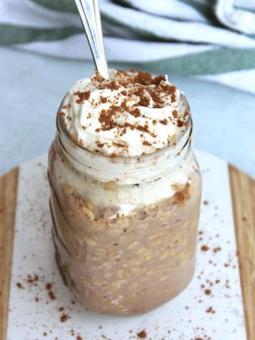 A spoon in a jar of overnight oats topped with whipped cream.