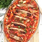 Sausage and bean casserole in a glass baking dish on a wooden chopping board.