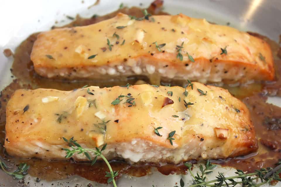 Close up of two baked salmon fillets garnished with fresh thyme.
