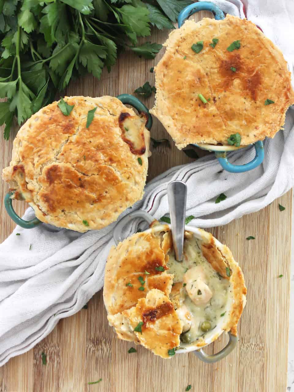 Three salmon pies on a wooden chopping board with fresh parsley.