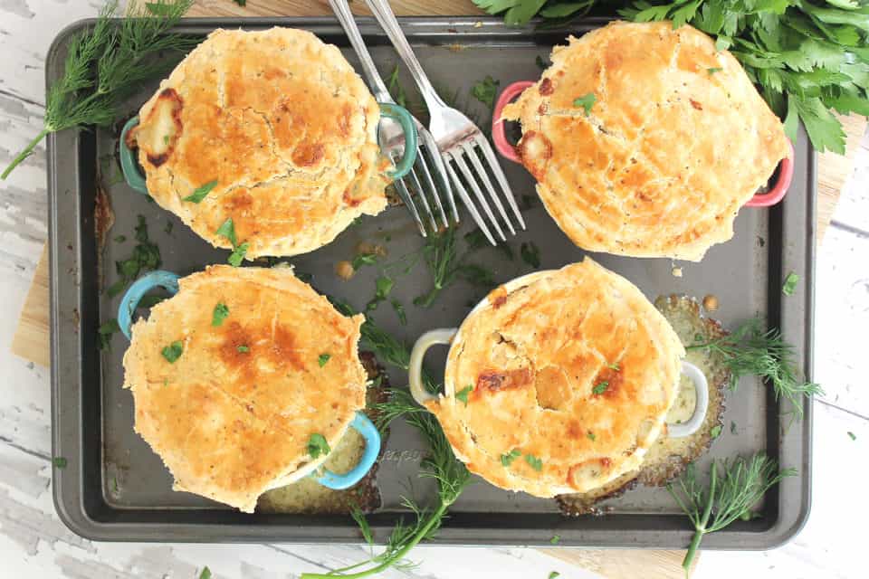Overhead shot of four baked salmon pies on a baking sheet with fresh dill.