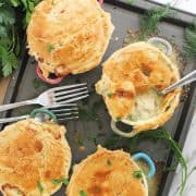 Four baked salmon pies on a baking sheet with a spoon in one of them.
