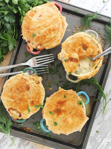 Four baked salmon pot pies on a baking sheet, garnished with fresh dill and parsley.