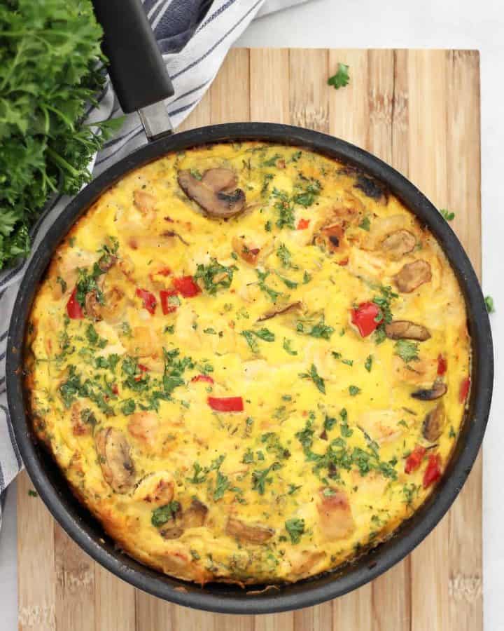 A chicken frittata in a skillet on a wooden chopping board.