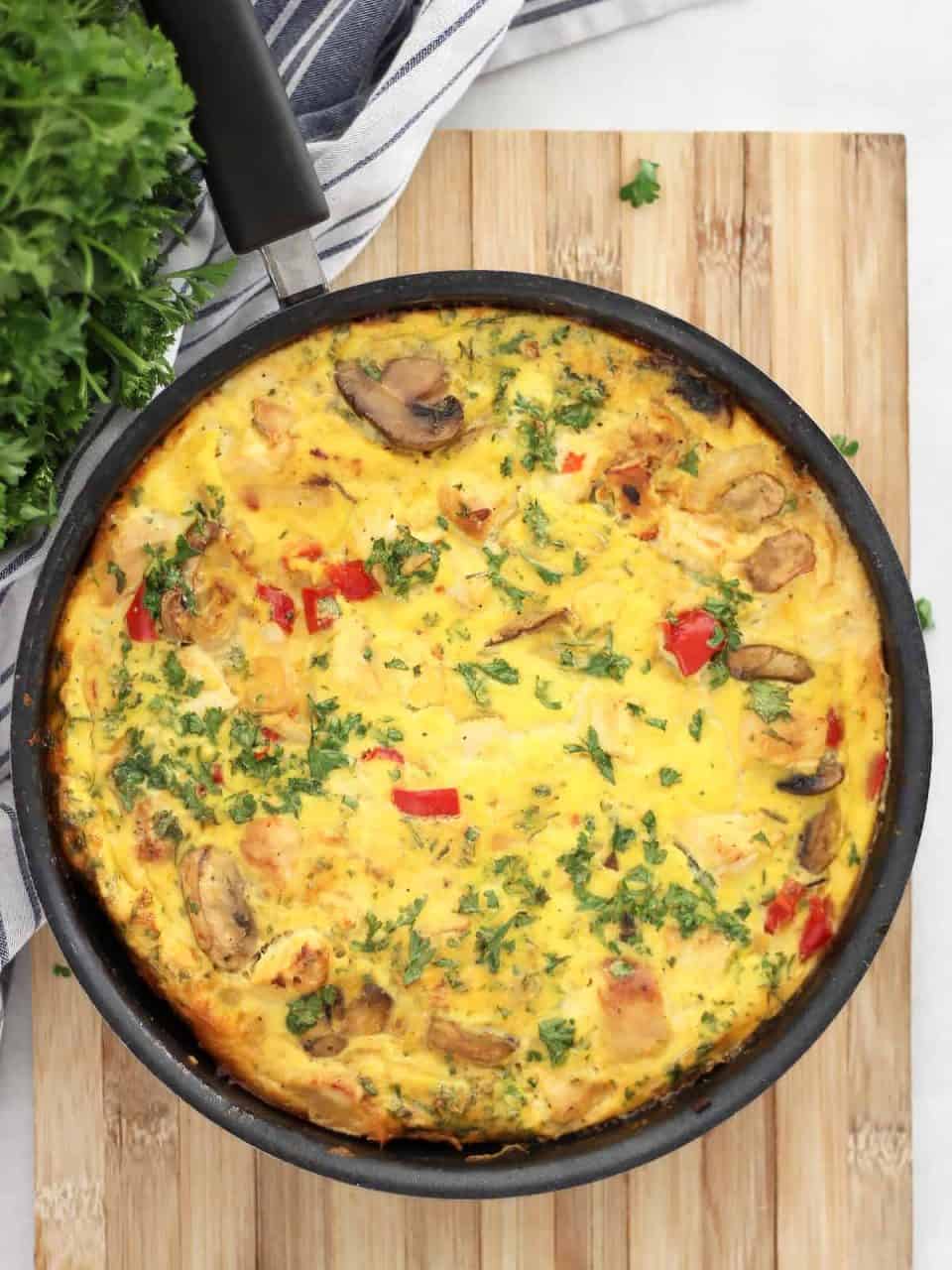 A chicken frittata in a skillet on a wooden chopping board.