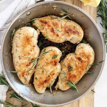 Four lemon rosemary chicken breasts in a skillet garnished with fresh herbs.