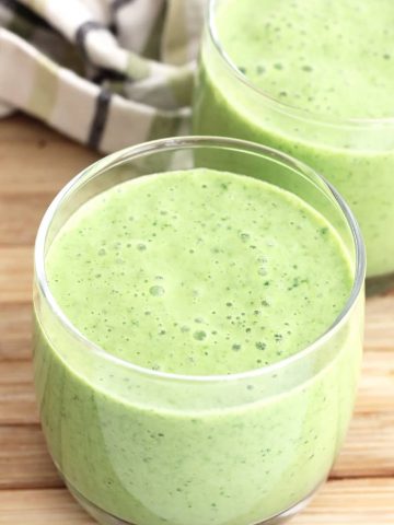 Two glasses of mango spinach smoothie next to a green and white cloth.