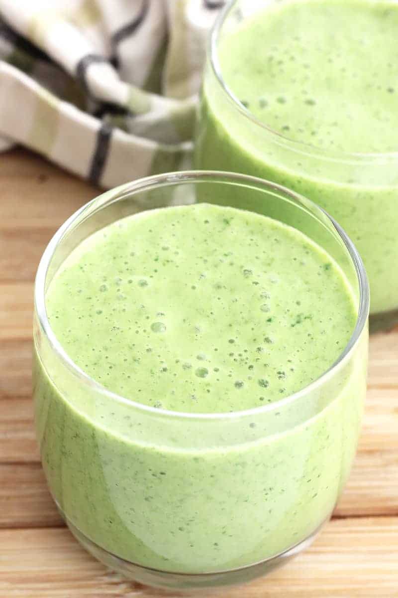 Two glasses of mango spinach smoothie next to a green and white cloth.