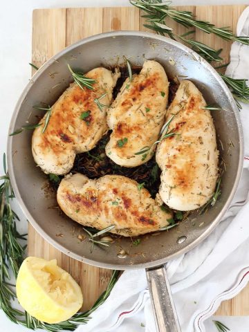 Four cooked lemon rosemary chicken breasts in a skillet.