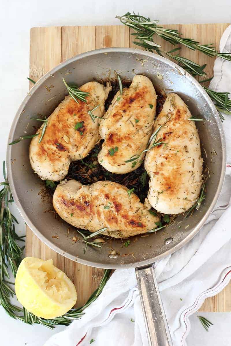 Four cooked lemon rosemary chicken breasts in a skillet.