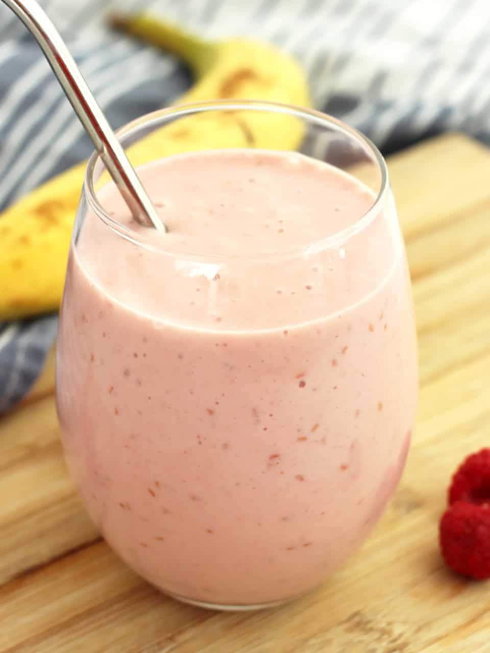 A raspberry banana smoothie in a tall glass next to fresh fruits.