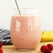 A raspberry banana smoothie in a glass with a straw.
