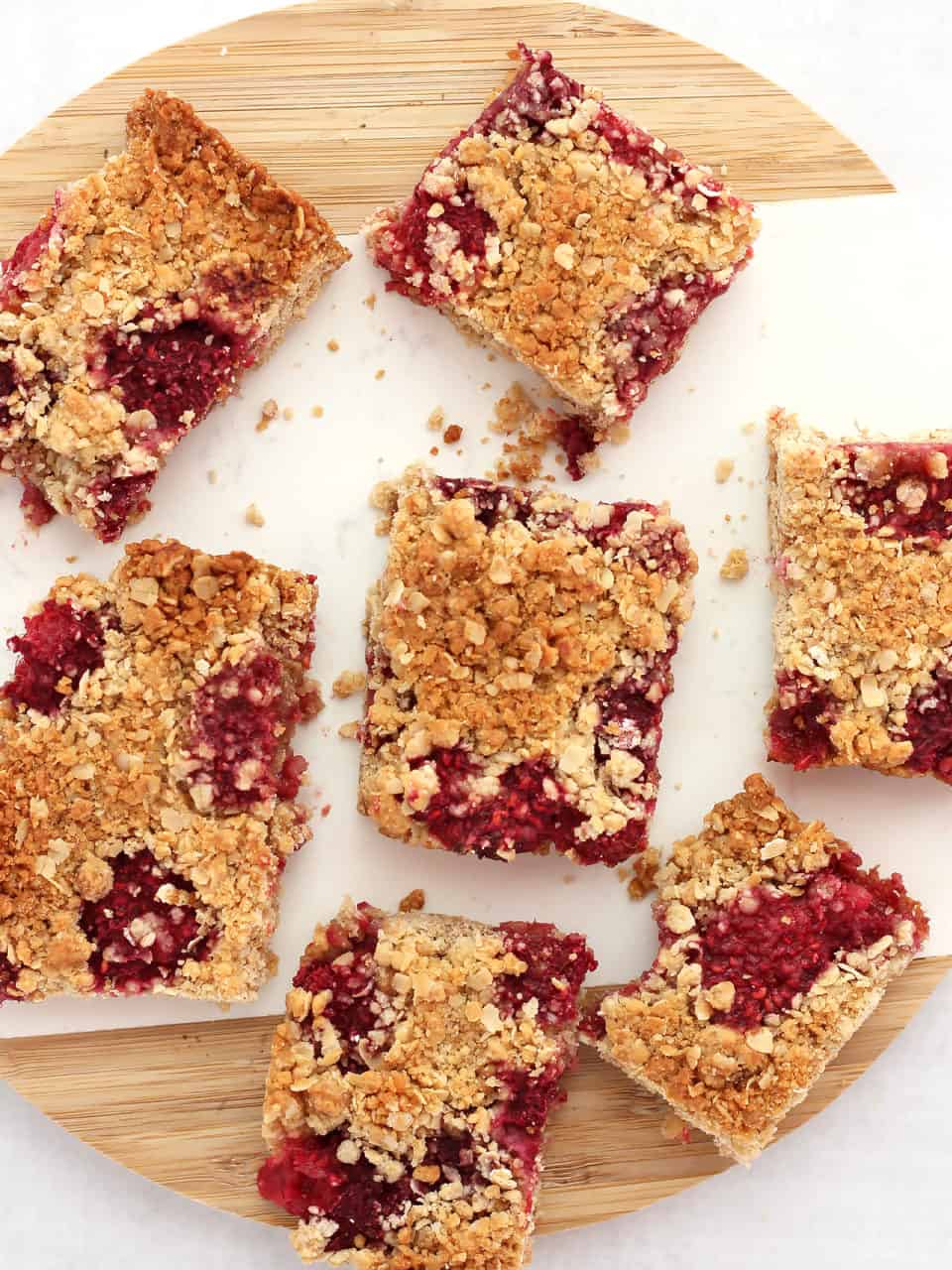 Seven oatmeal bars with raspberries on a wood and marble cutting board.