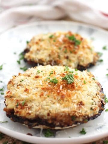Two stuffed mushrooms on a plate garnished with fresh herbs.